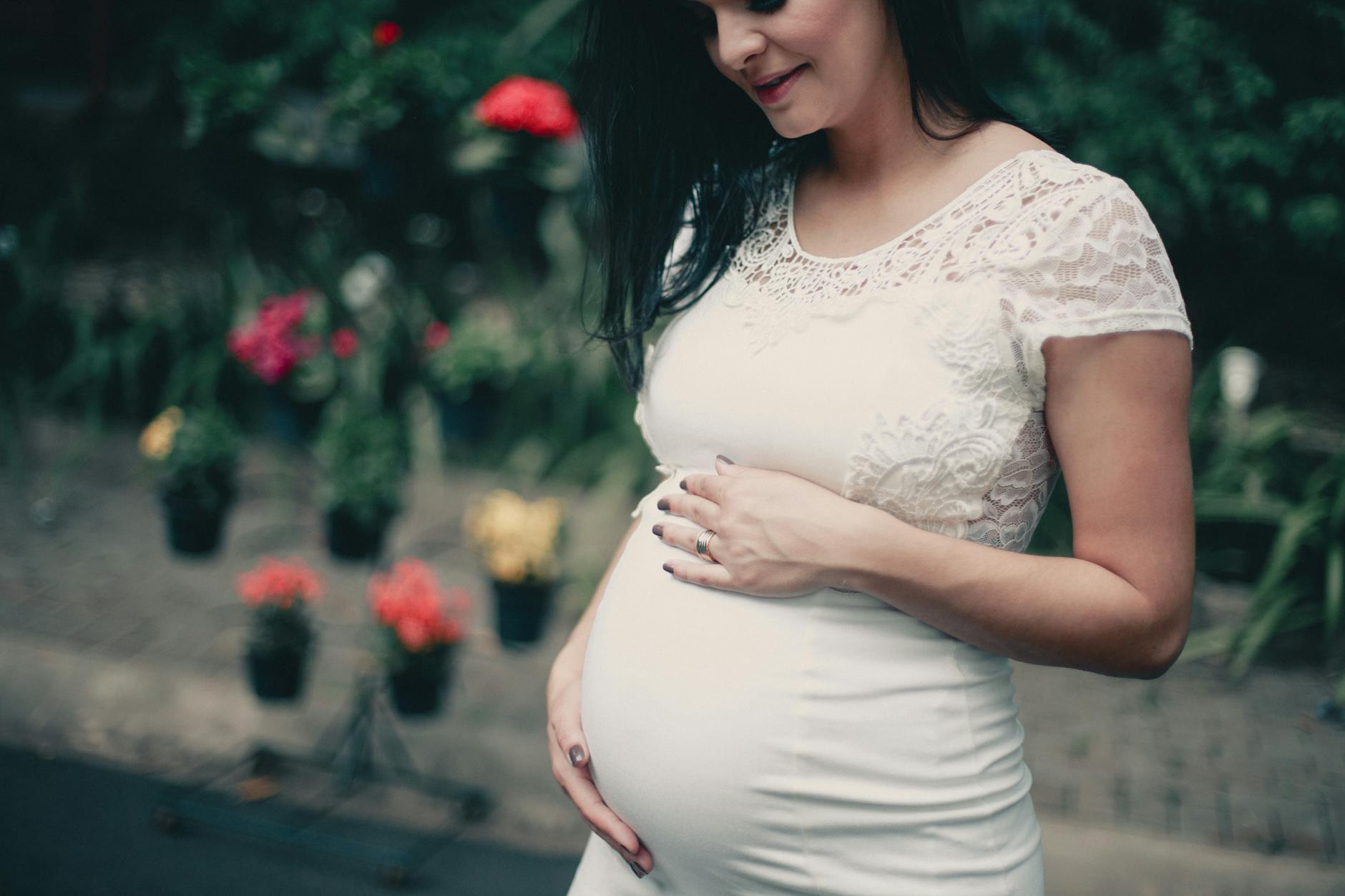 close up photo of pregnant woman in white dress holding her stomach